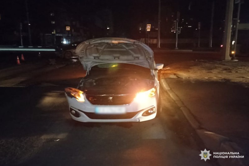 Легковий автомобіль стоїть на дорозі з піднятим капотом, увімкнені фари та аварійна сигналізація.