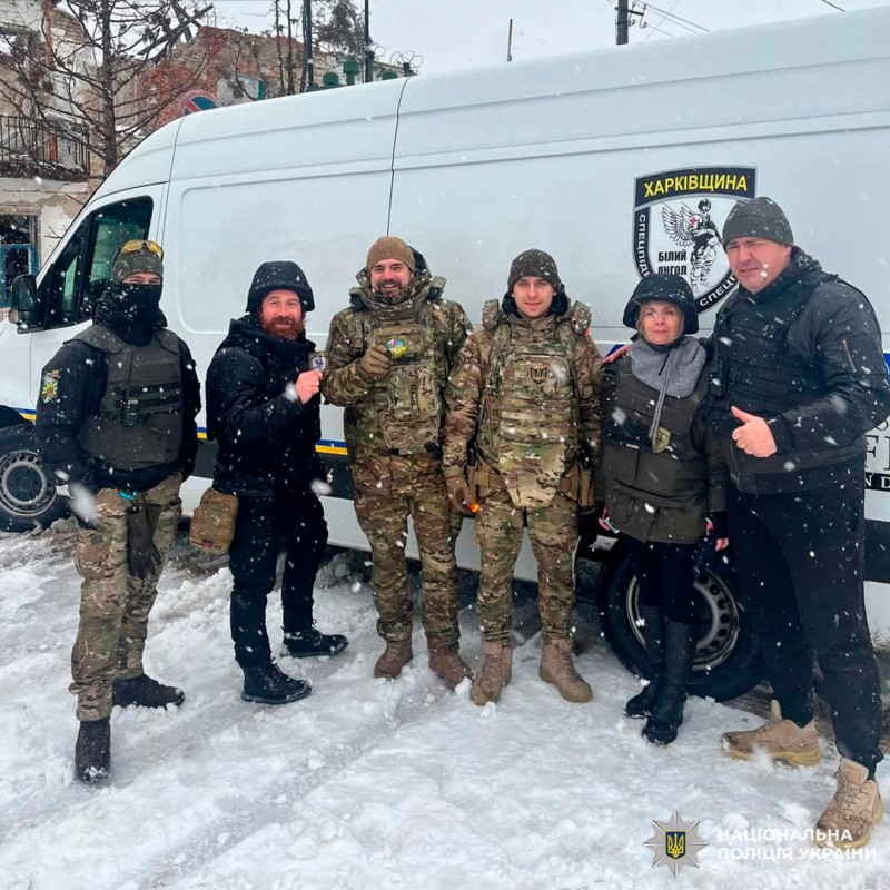 Шестеро людей стоять біля поліцейського мікроавтобуса Харківщини на засніженій вулиці.