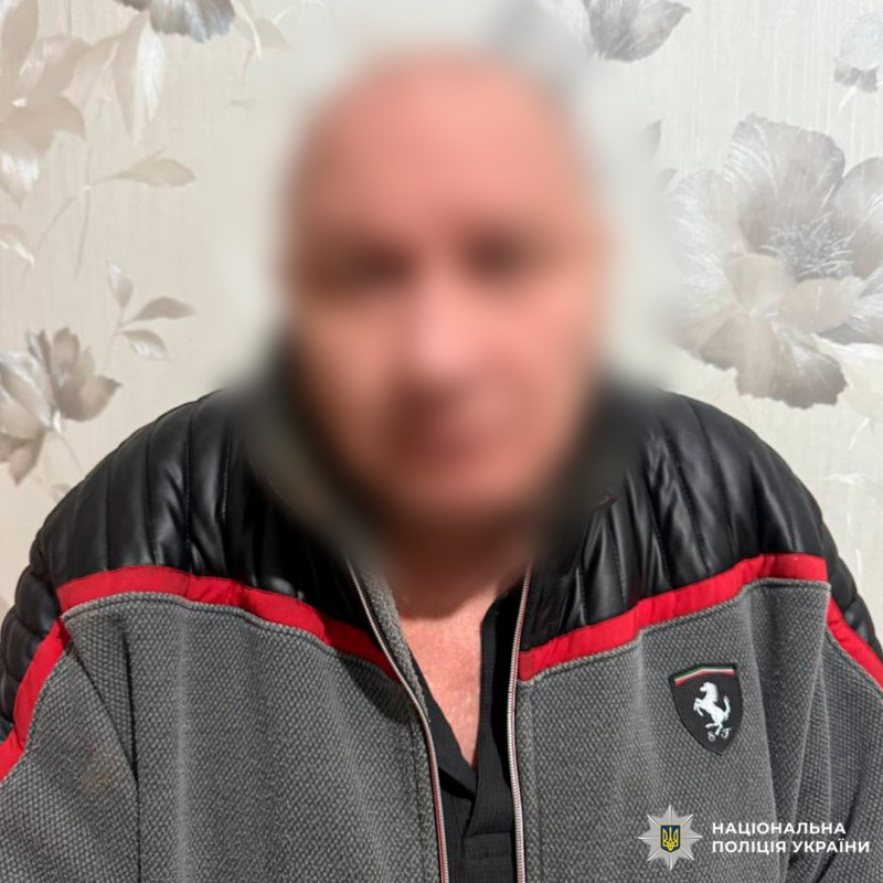 Чоловік у куртці Ferrari на фоні квітчастих шпалер.