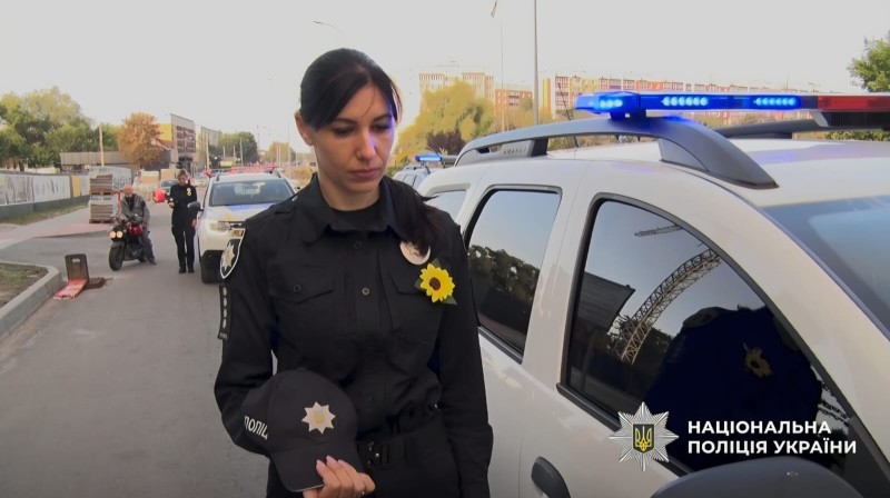 На фото поліцейська, яка стоїть біля службового автомобіля під час хвилини мовчання.