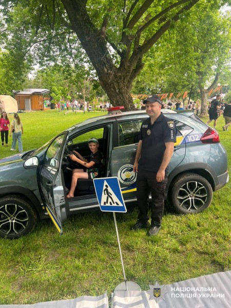 На фото у слубовому автомобілі за кермом сидить хлопчик, а поряд стоїть поліцейський.