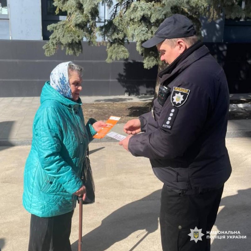 На фото зображено офіцера Національної поліції України, який спілкується з літньою жінкою на вулиці.