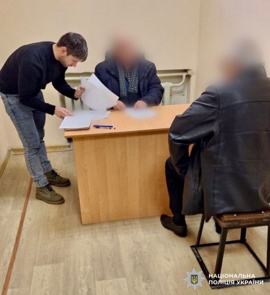 На фото затриманий та поліцейський у приміщенні.