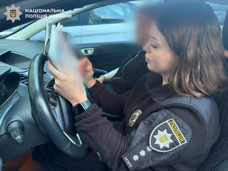 На фотографії зображено поліцейську, яка складає адміністративні матеріали на правопорушницю.