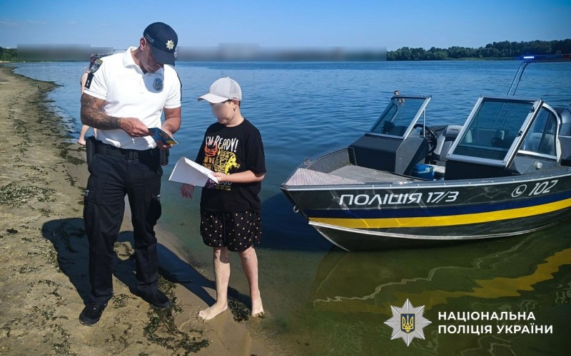 На березі Дніпра водний поліцейський спілкується з дитиною про правила безпеки на воді