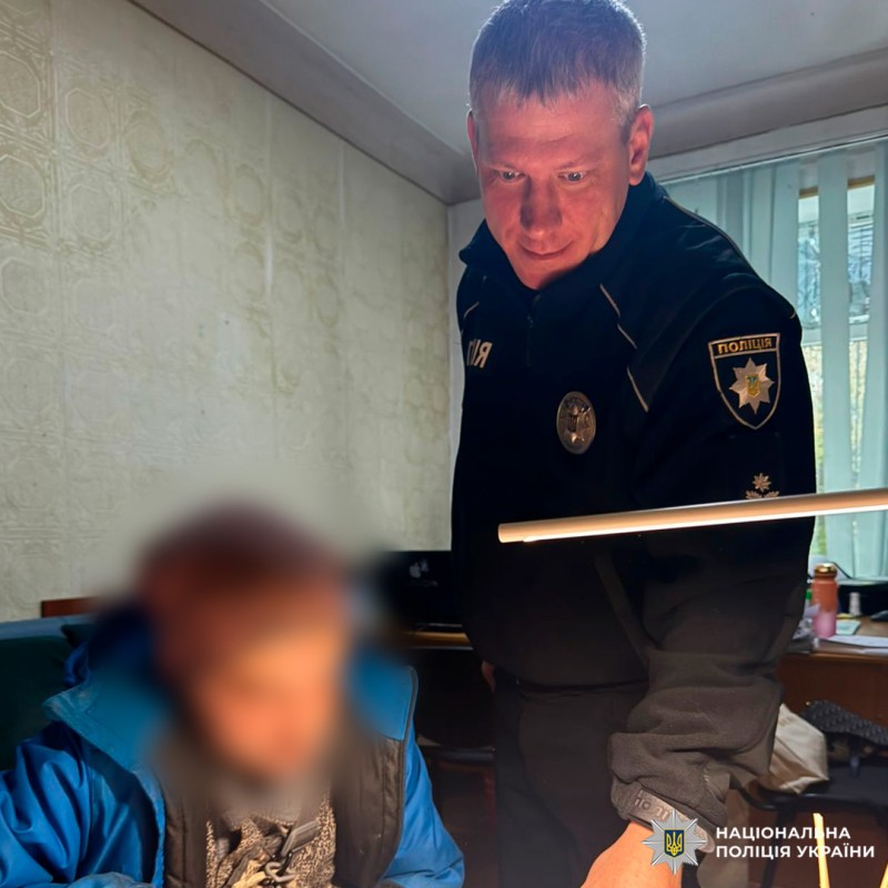 Поліцейський у формі пояснює документ особі в куртці, яка уважно читає його за столом. На фоні ноутбук, лампа.