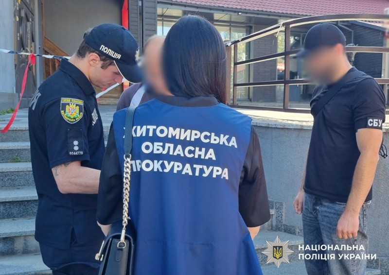 на передньому плані спиною стоїть жінка прокурор, зліва поліцейський боком, який врущає фігуранту підозру, зправа стоїть працівник СБУ