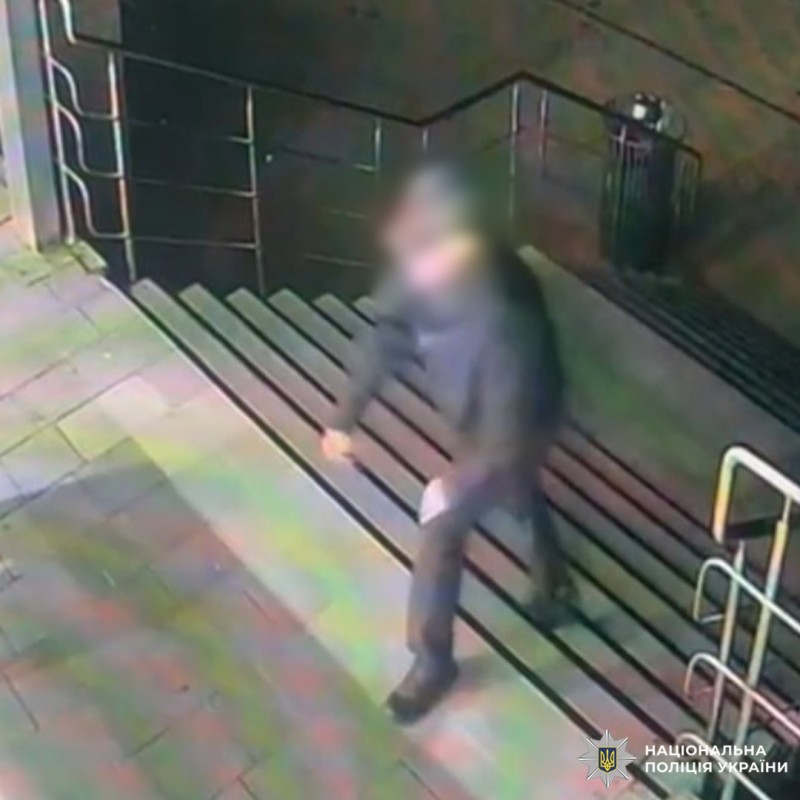 Кадр із камери спостереження: особа в темному одязі підіймається сходами на вулиці вночі. Обличчя розмито з метою захисту персональних даних. На фоні плитка, металеві поручні та темна стіна.