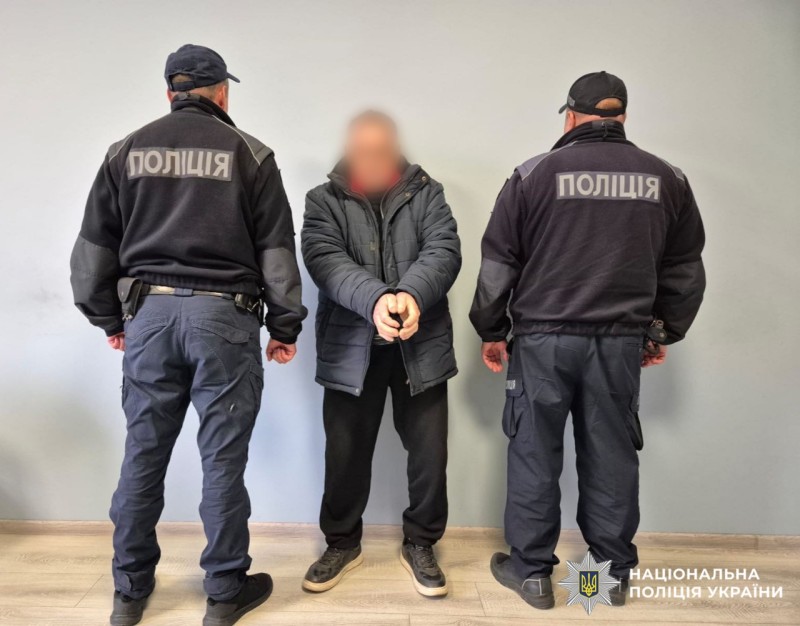 на фото зображений затримаий у наручниках, обличчям. По обидва боки від нього стоять поліцейські спиною. .