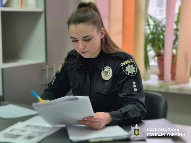 Офіцерка поліції опрацьовує паперові документи, сидячи за столом