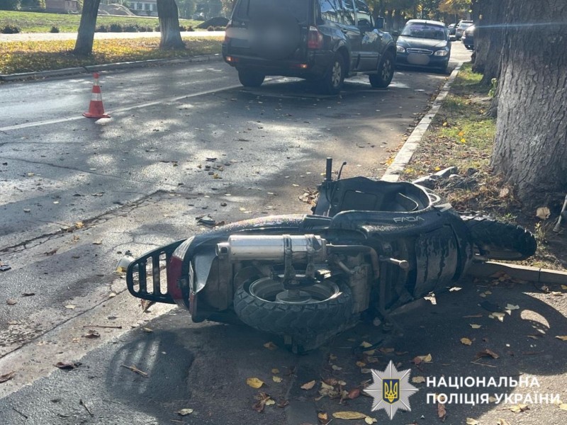 На фото скутер, який лежить на узбіччі дороги.