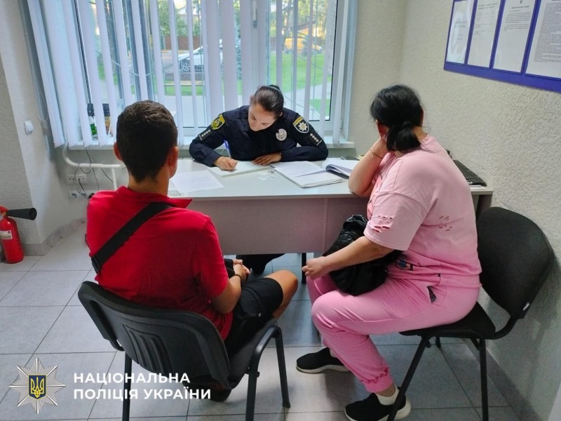 На фотографії зображено поліцейську Київщини, яка складає адміністративні матеріали на батьків неповнолітнього за зняття шевронів з інсталяції на Бучанщині.