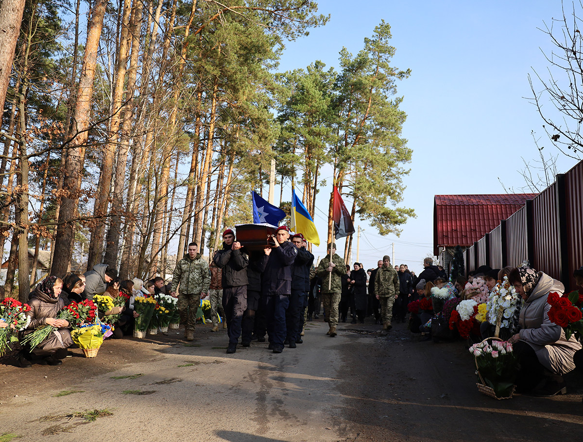 Поліцейськіі несуть труну. Люди по обидва боки дороги стоять на колінах із квітами, віддаючи шану загиблому.