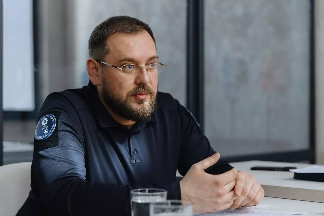 Артур Добросєрдов сидить за столом, на якому лежать папери, два стакани з водоюн
