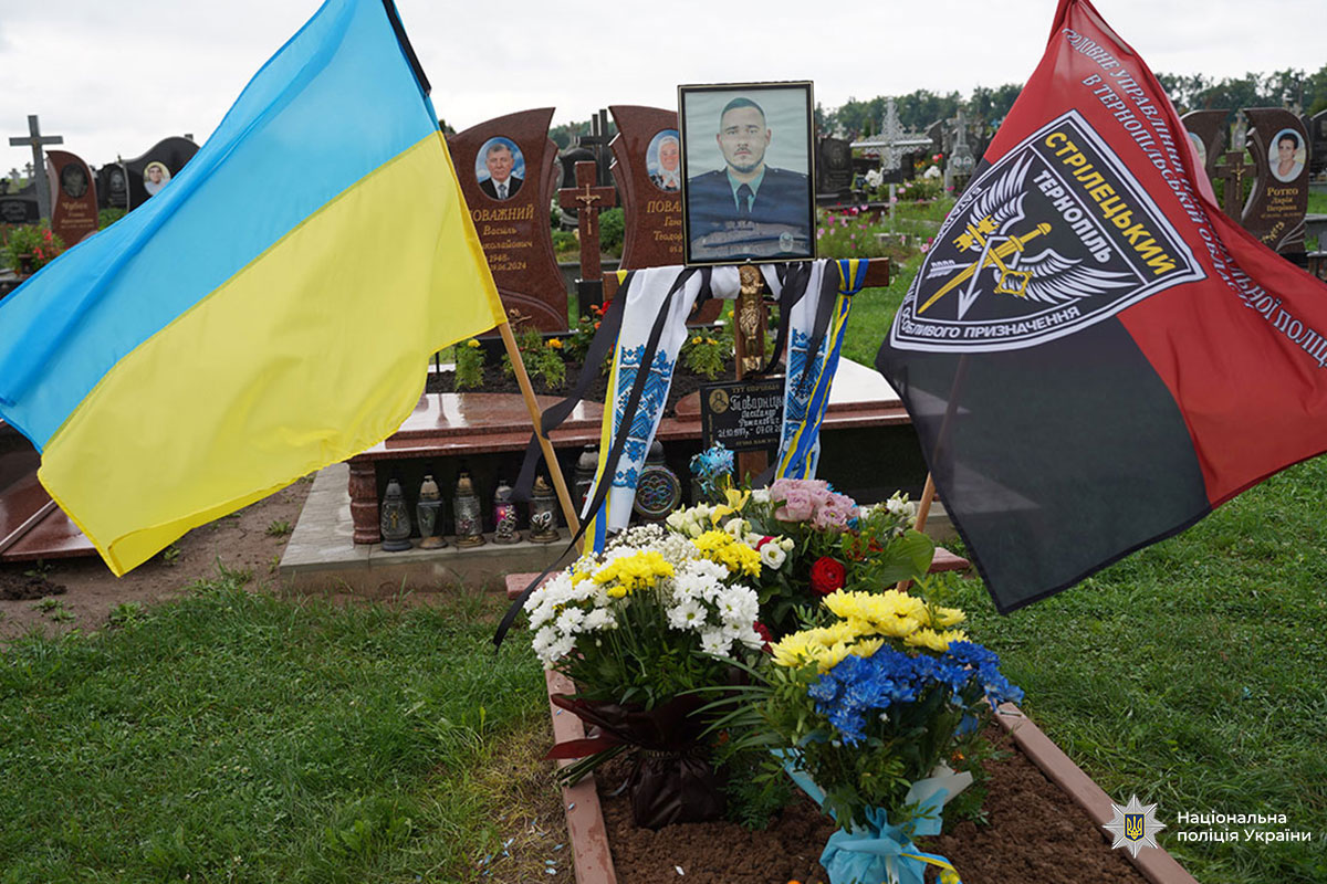 Могила поліцейського з синьо-жовтим прапором України, прапором підрозділу. На могилі - його фотографія та багато квітів.