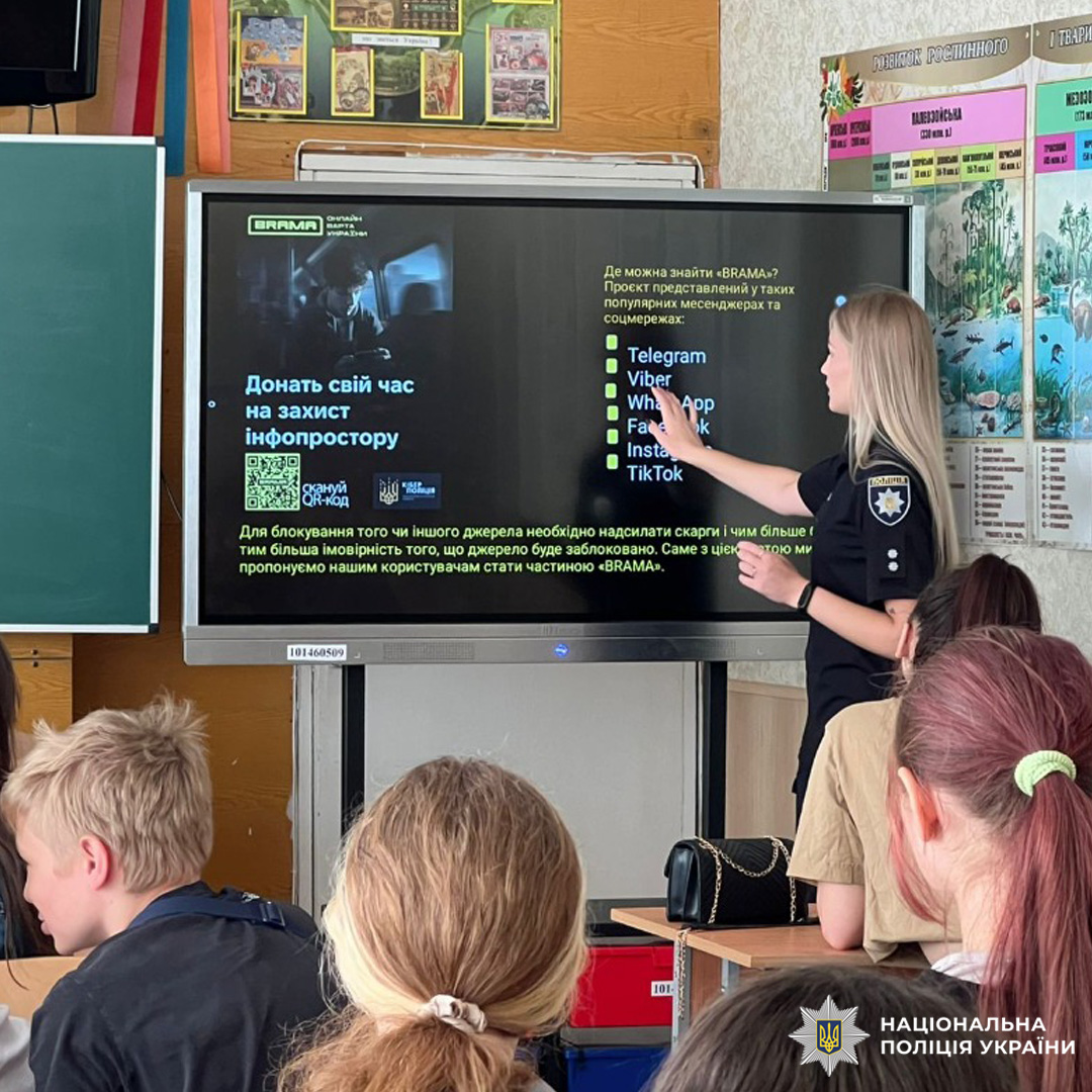 Вчитель у формі поліції проводить урок для учнів, показуючи на екрані QR-код та список додатків у соцмережах.