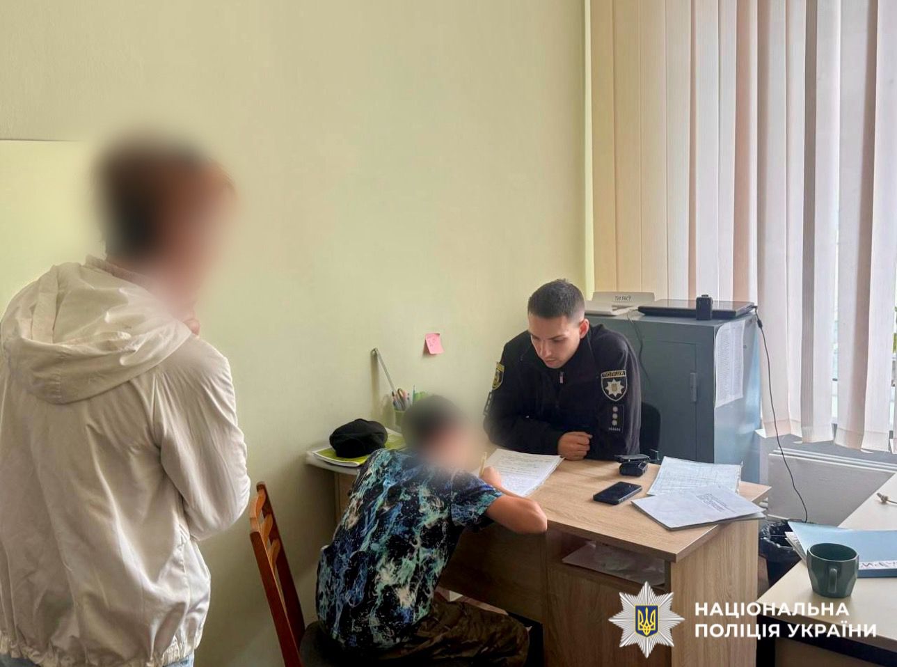 На фото зображено поліцейського, який в кабінеті проводить профілактичну бесіду та складає адміністративні матеріали на батьків неповнолітнього, що їздив на тролейбусі ззовні, наражаючи себе на небезпеку
