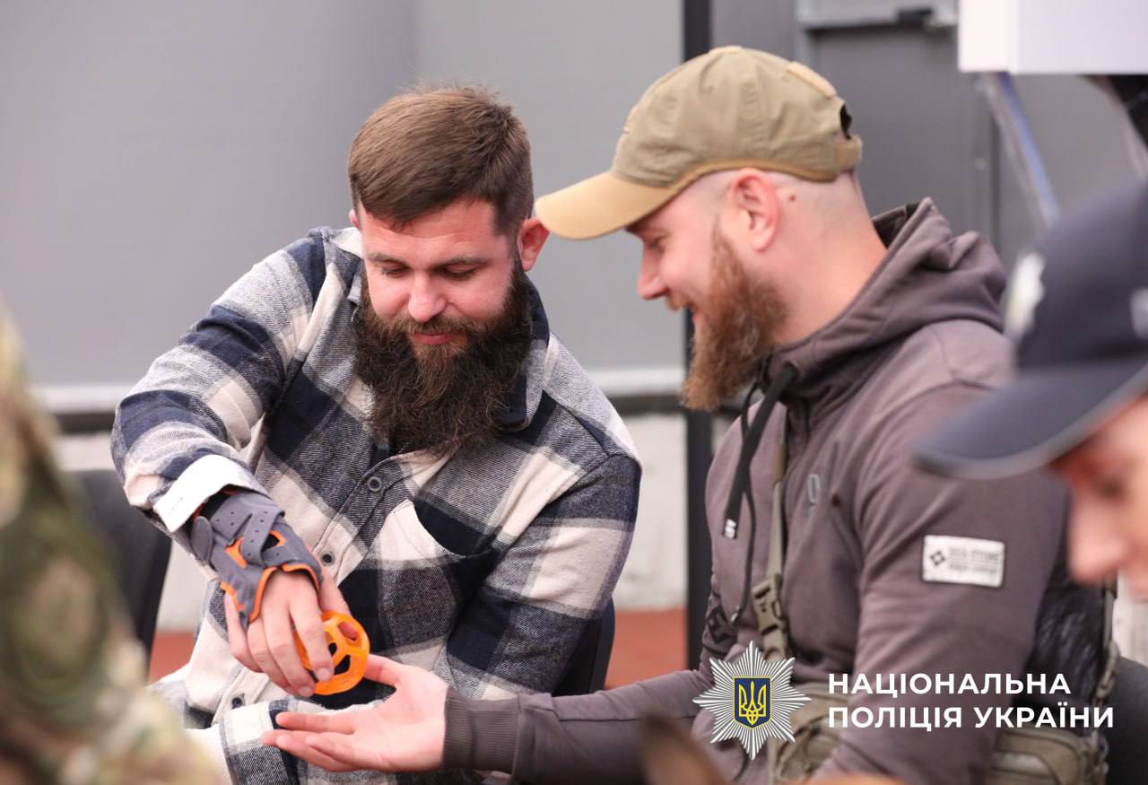 На фото зображені 2 учасника зустрічі, які сидять поруч один з одним та на прохання кінолога передають один одному м`ячик.