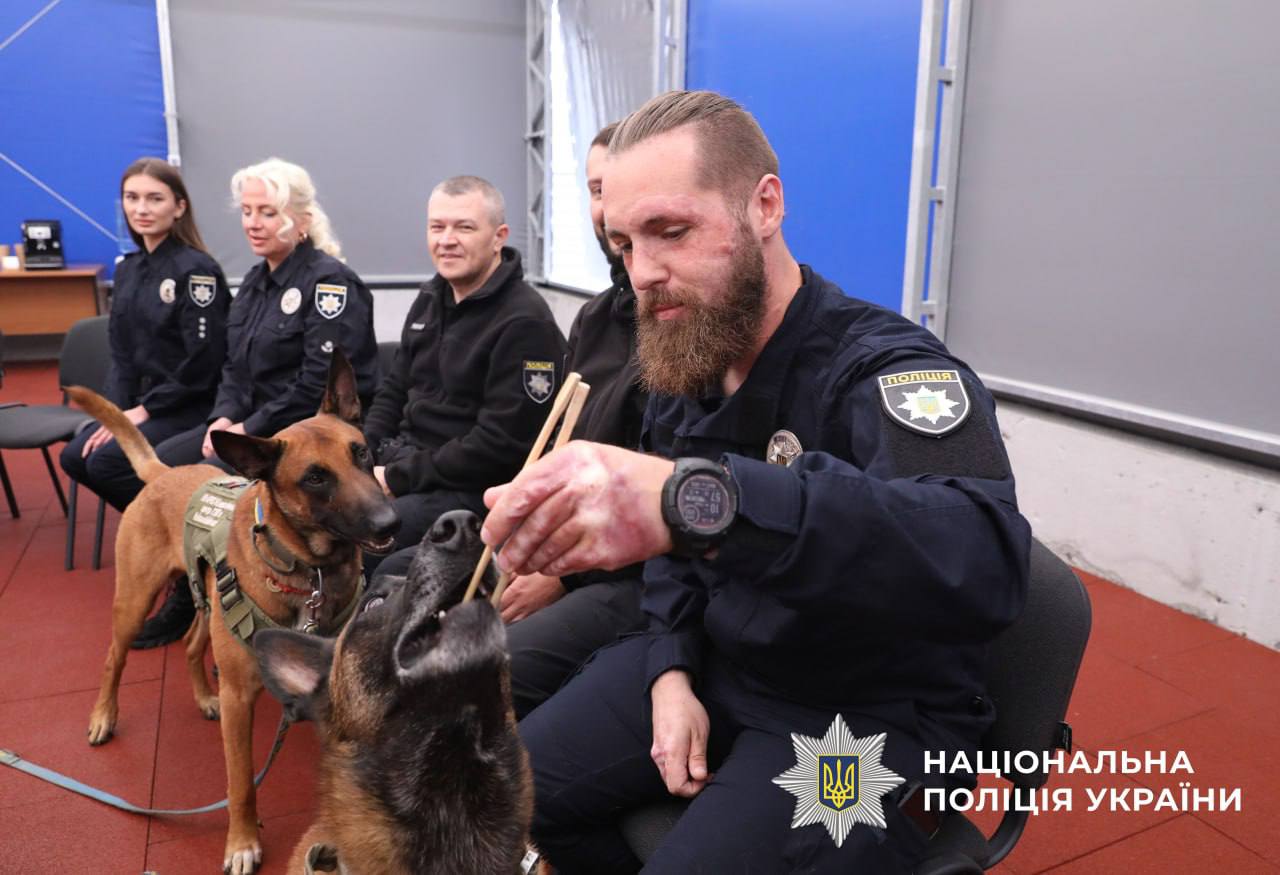 На фото зображений поліцейський який годує собаку паличками для суші