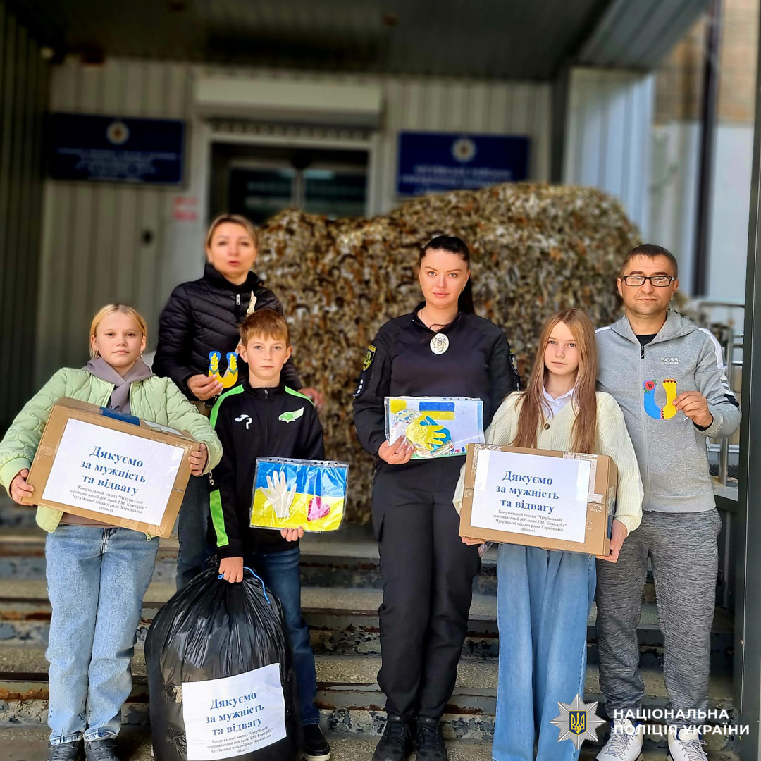 діти та поліцейська, тримають коробки з дитячими малюнками та виробами з написами "Дякую за мужність та відвагу", на фоні будівлі поліції.