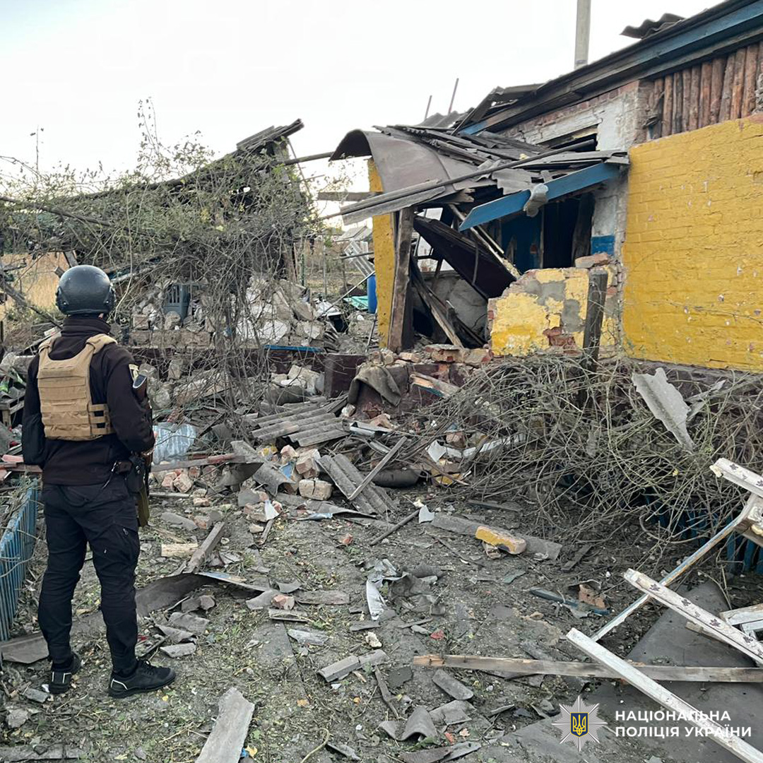зруйнований будинок рядом стоїть поліцейський.