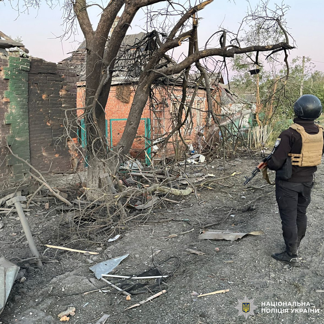 зруйнований будинок рядом стоїть поліцейський.