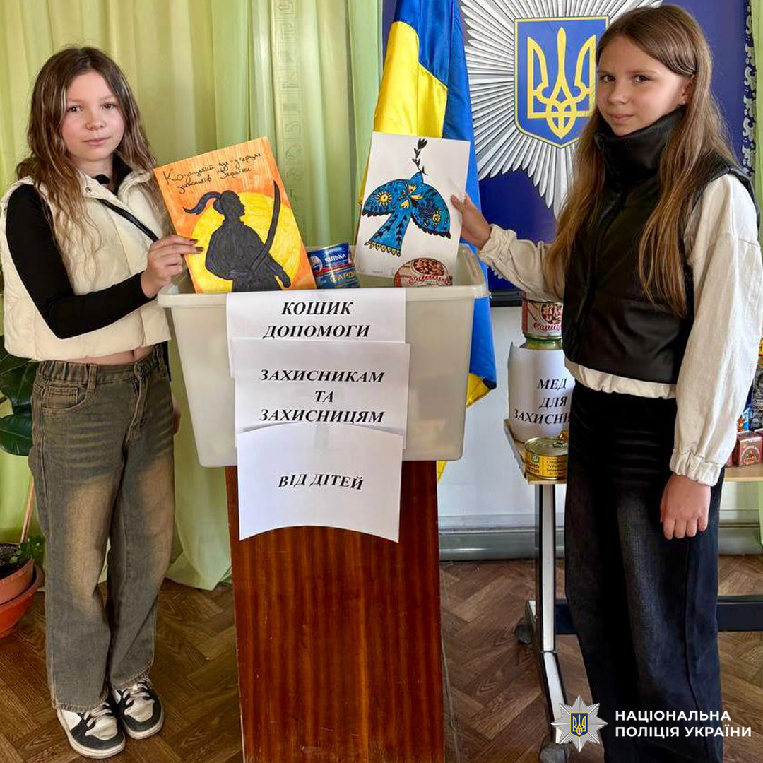 Діти біля коробки з написом "Кошик допомоги захисникам", тримають малюнки; поруч прапор України