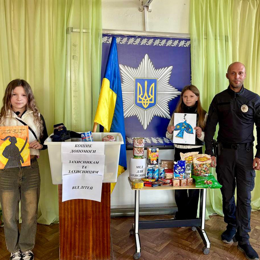 Двоє дітей передають малюнки та продукти для військових, поруч поліцейський та прапор України.