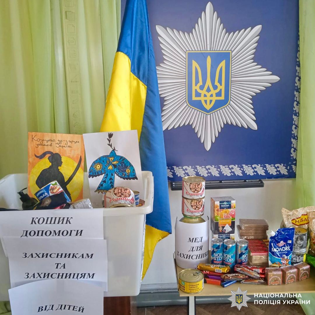 Стенд для захисників: коробка з дитячими малюнками, їжа, мед; поруч прапор України та емблема Нацполіції.