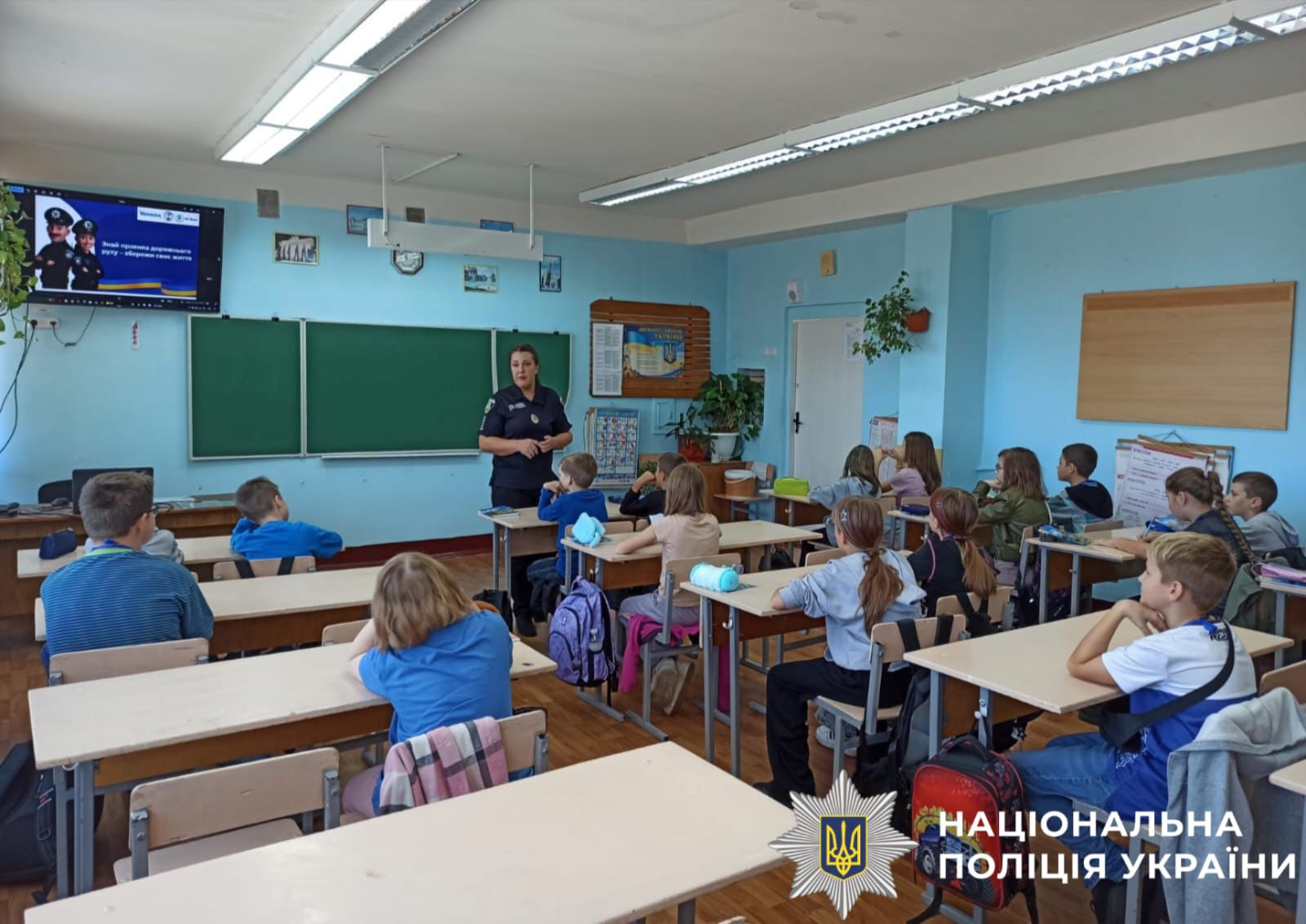 На фото зображений клас, дти сидять за партами. Поліцейський стоїть біля дошки та розповідає зазначені у статті теми.