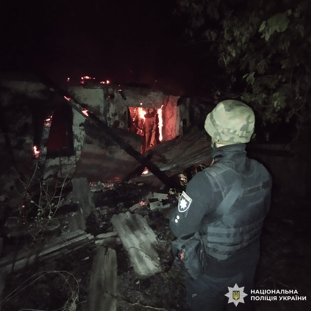 Поліцейський у бронежилеті стоїть перед палаючою будівлею вночі.