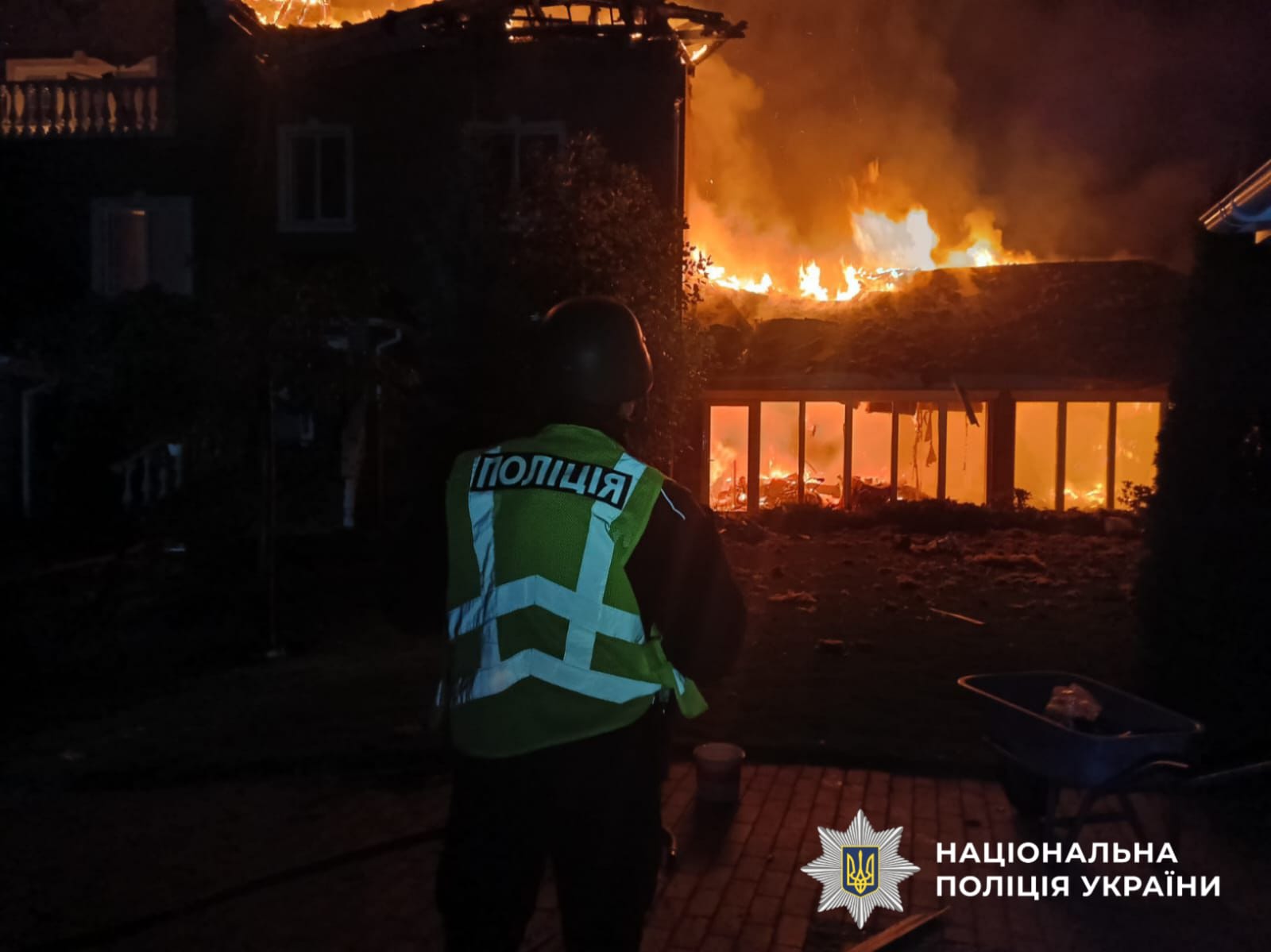 На фото зображений поліцейський, який стоїть спиною, на фоні палаючої будівлі. Фото з місця влучання.