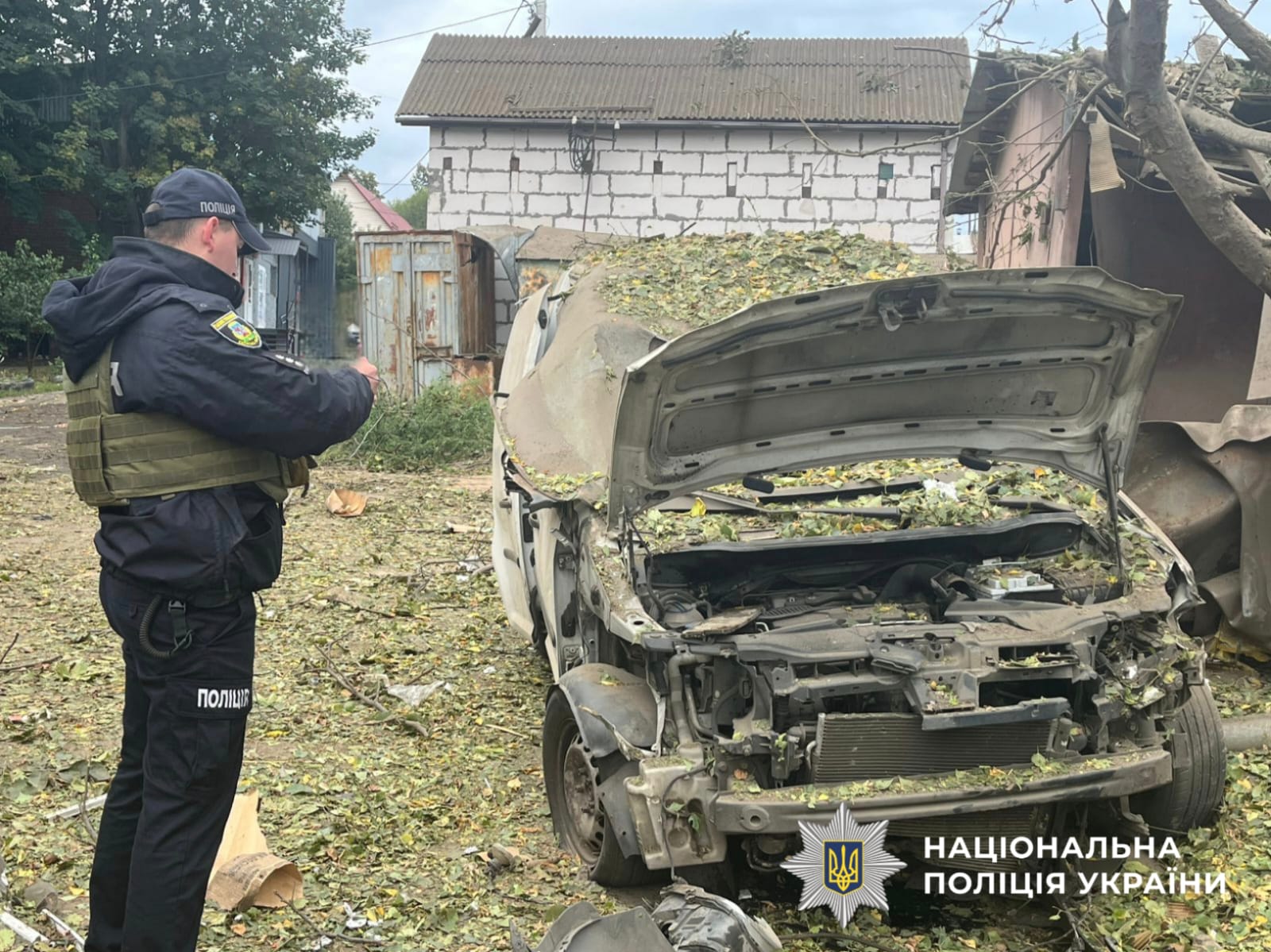 На фото зображений поліцейський на фоні пошкодженої автівки. Фото зроблене на місці події, під час документування воєнного злочину