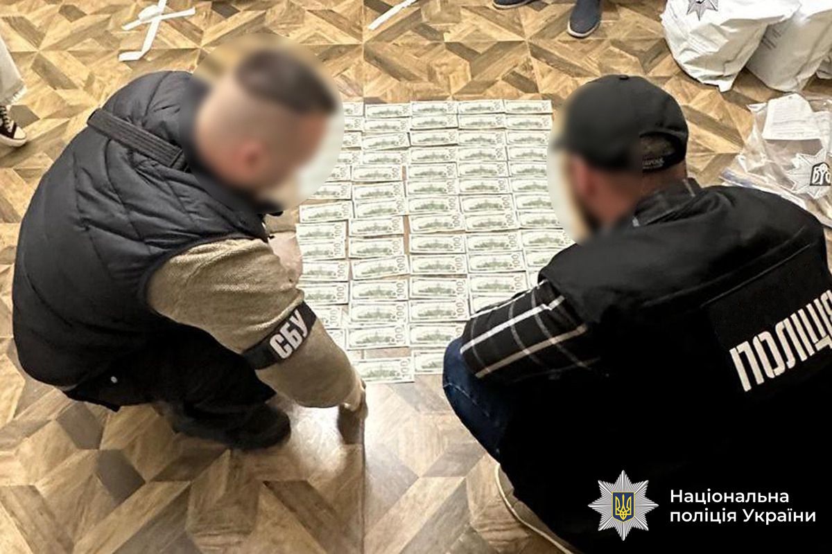 Поліцейський та працівник СБУ знаходяться біля розкладених на підлозі грошей, вилучених під час обшуку