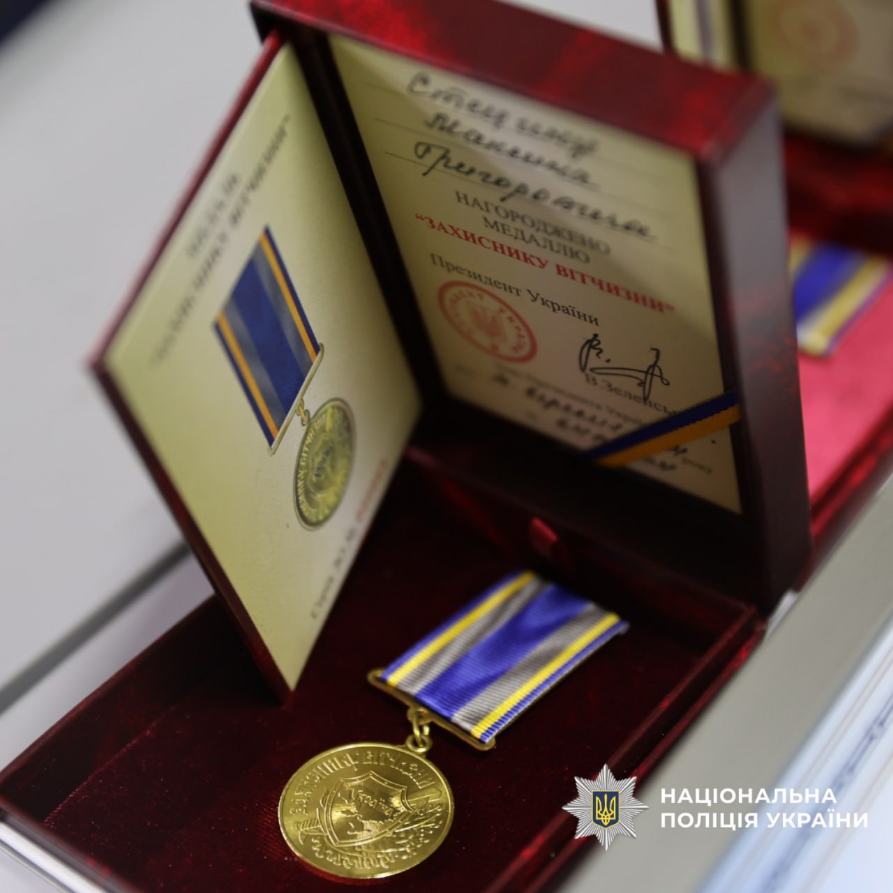 Медаль "Захисник Вітчизни" у червоній оксамитовій коробці з сертифікатом, підписаним Президентом України. Медаль золотого кольору з синьо-жовто-білою стрічкою.