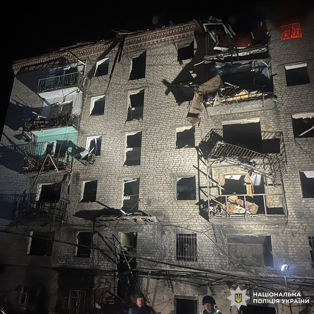 Зруйнована багатоповерхівка вночі: вибиті вікна, обвалені балкони, уламки на фасаді.
