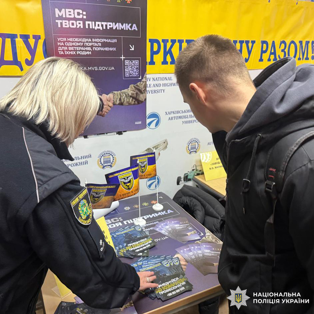 Поліцейська у формі спілкується з молодим чоловіком. На столі  буклети,банер із написом МВС: Твоя Підтримка.