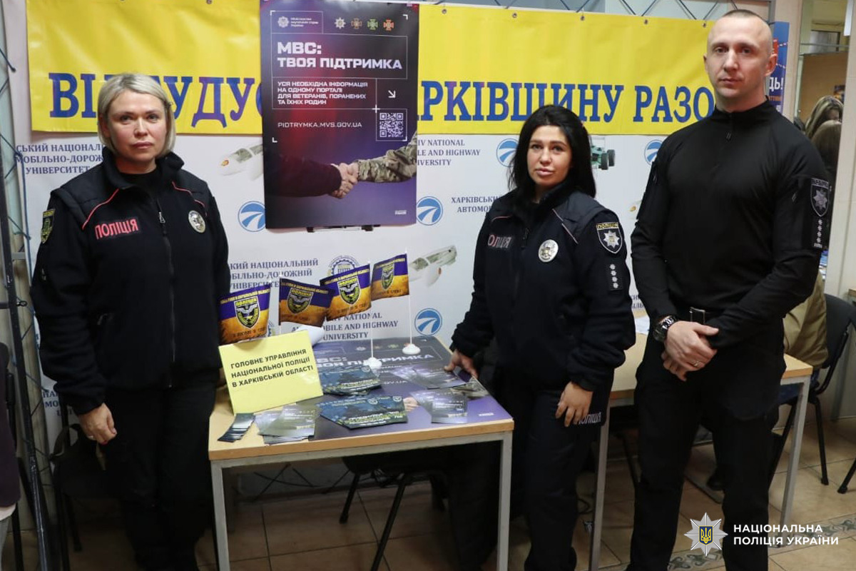 Троє поліцейських у формі стоять за столом із буклетами. На банерах гасло Відбудуємо Харківщину разом і МВС: Твоя Підтримка.