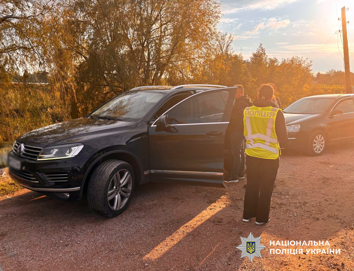 Поліцейська та правопорушник стоять поблизу чорного автомобіля
