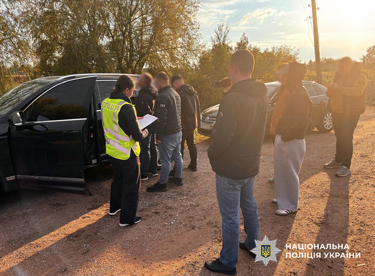 поліцейські та СБУ затримують правопорушника поблизу чорного автомобіля. поліцейська тримає в руках документи, інший правоохоронець знімає дії поліції та СБУ на камеру