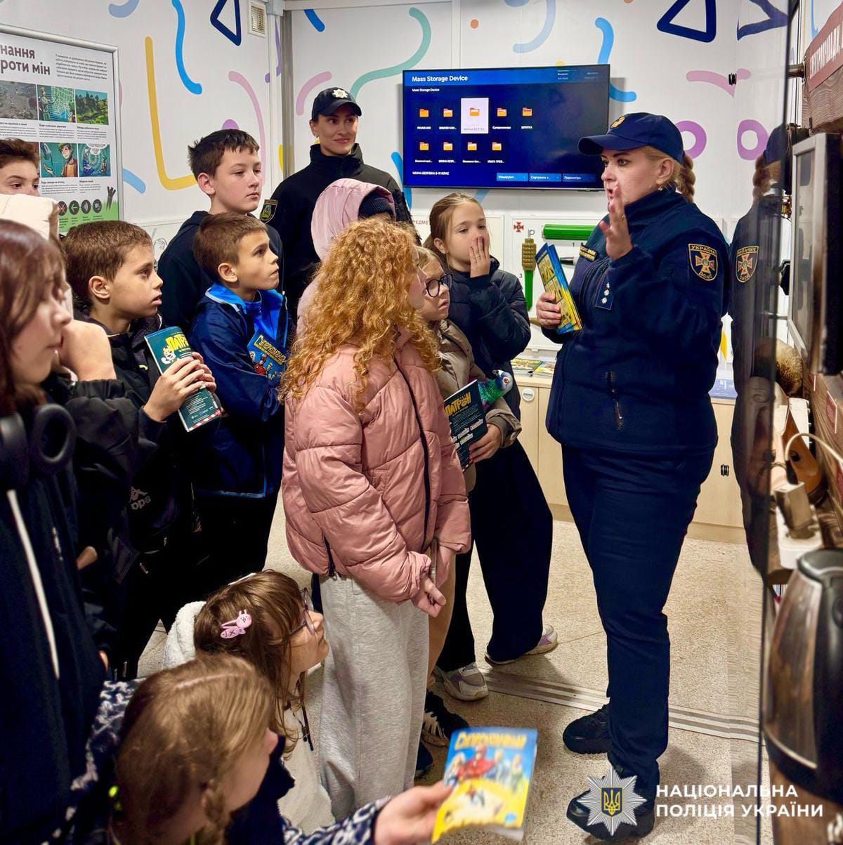 Діти та поліцейська стоять у мобільному класі безпеки та спілкуються.