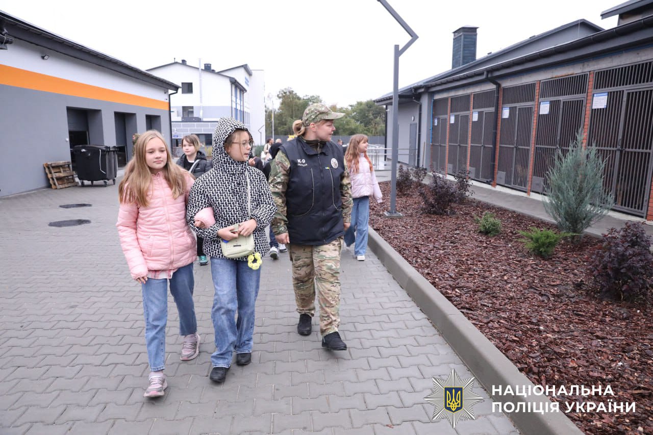 Кінолог та відвідувачі йдуть повз вольєрів, на території кінологічного центру.