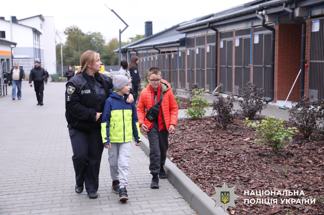 Поліцейська та діти йдуть територією кінологічного центра, вздовж вольєрів.