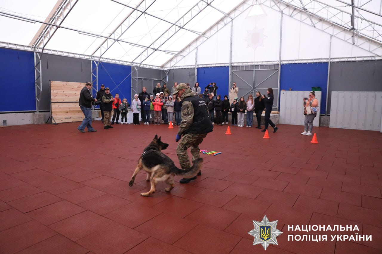 Всі учасники зустрічі спостерігають як слудбовий собака виконує команди кінолога.