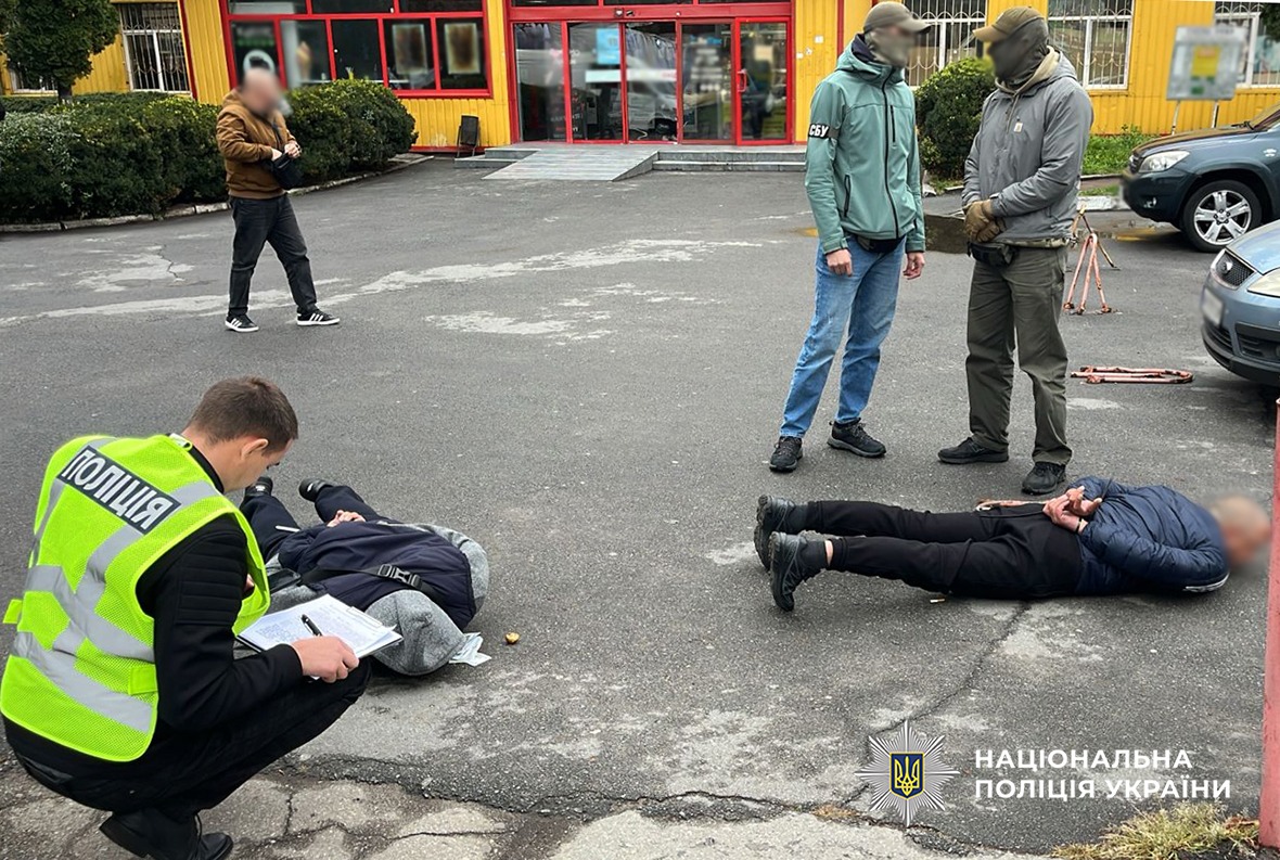 Поліцейські та співробітники УСБУ в області працюють на місці затримання двох фігурантів. Фігуранти лежать на асфальтному покритті