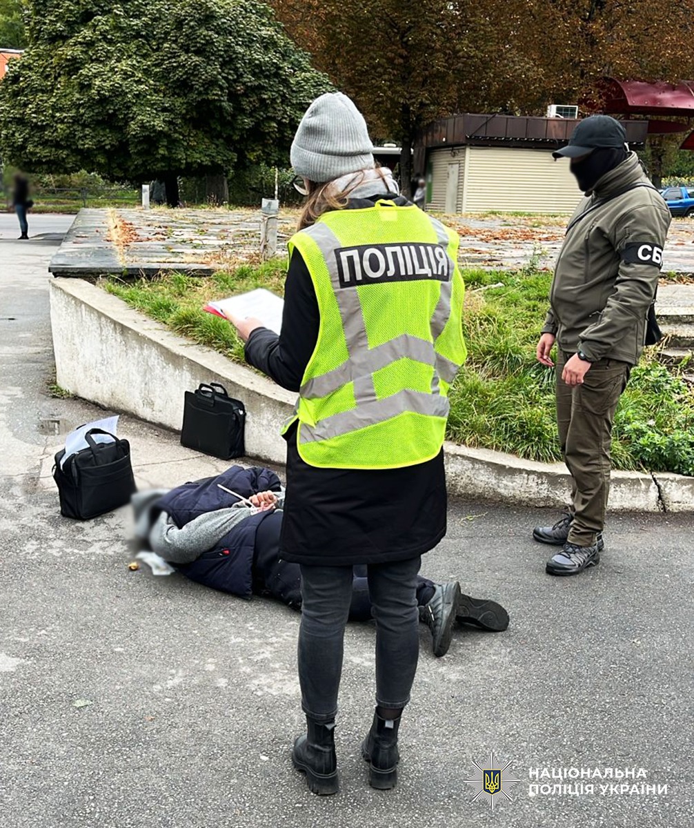 Поліцейська та співробітник УСБУ в області працюють на місці затримання двох фігурантів. Фігурант лежить на асфальтному покритті