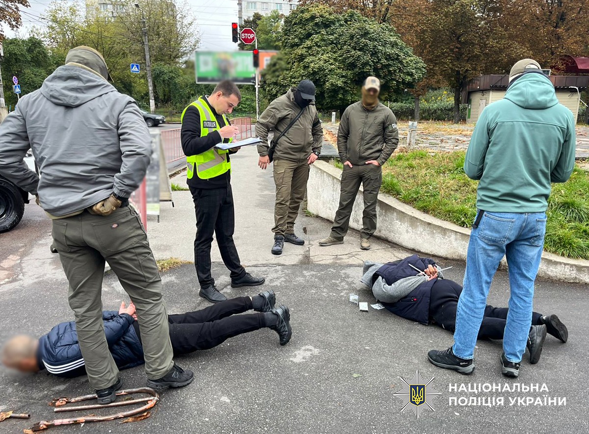 Поліцейські та співробітники УСБУ в області працюють на місці затримання двох фігурантів. Фігуранти лежать на асфальтному покритті