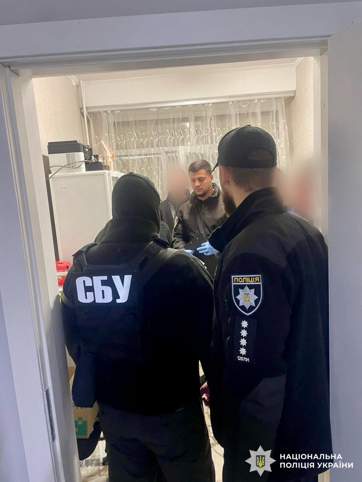 На фото зображені працівники поліцїі та СБУ, які проводять обшук у фігуранта.