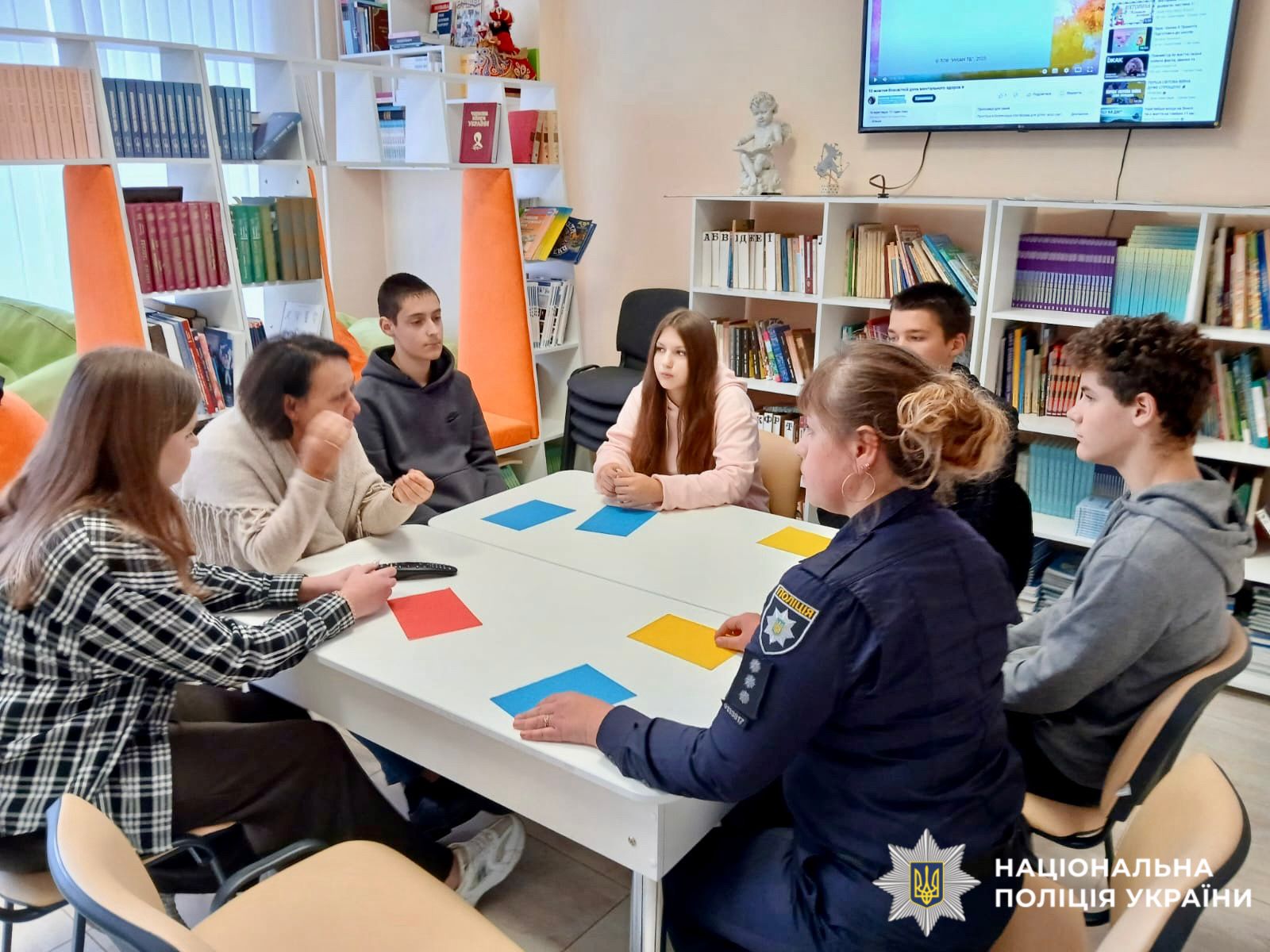 На фото зображені діти та поліцейська, які сидять за партою та спілкуються.