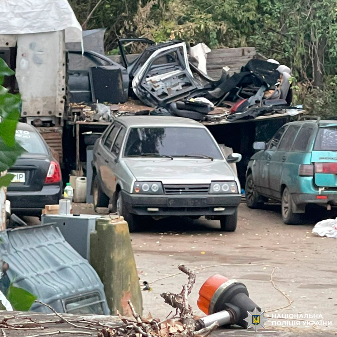 Автосервіс або розбірка з кількома старими машинами й купою автозапчастин, серед яких сірий ВАЗ-2109 на передньому плані.